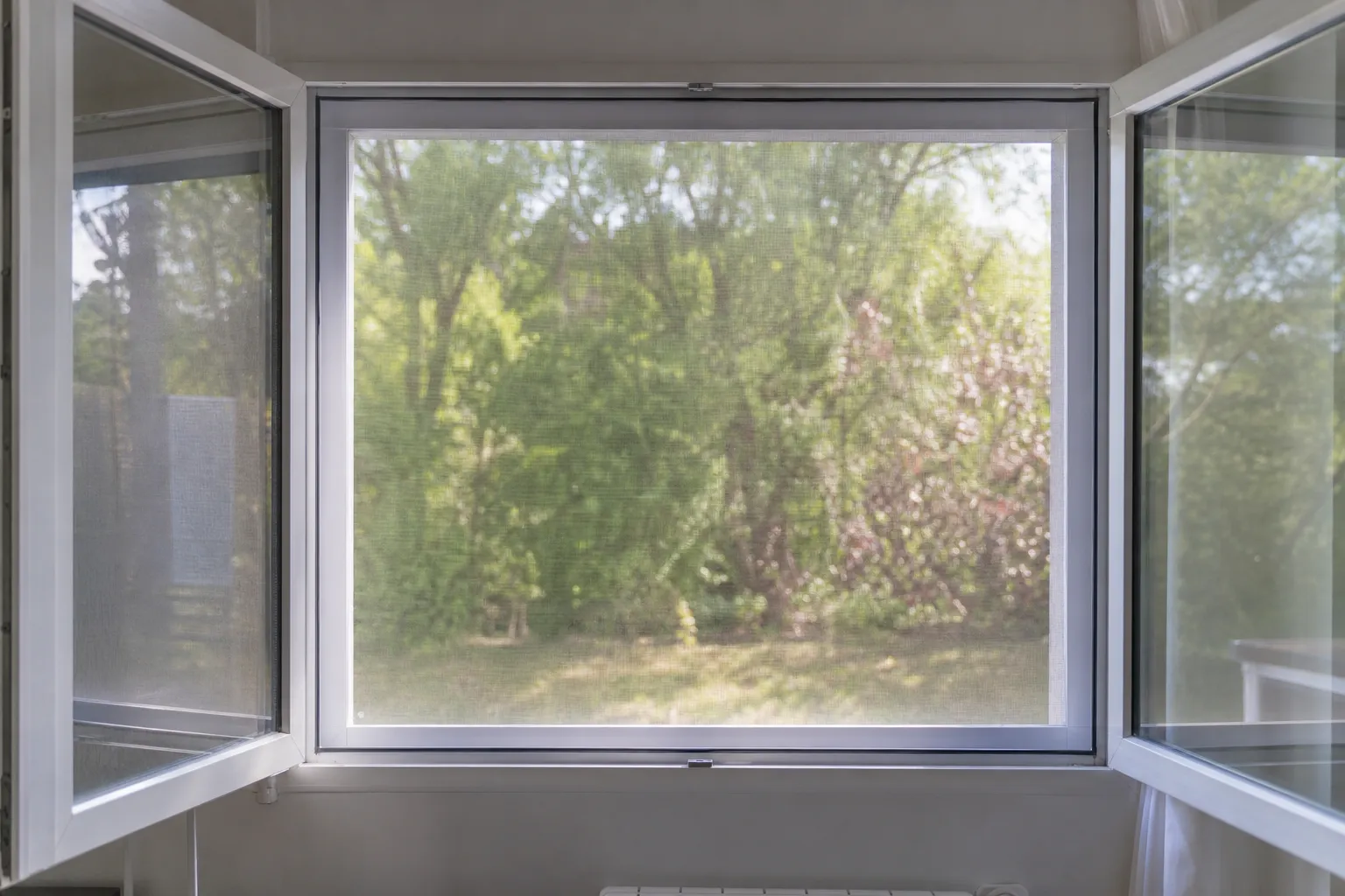 Moustiquaire à cadre fixe posée sur une fenêtre à battants ouverte, jardin visible en flou